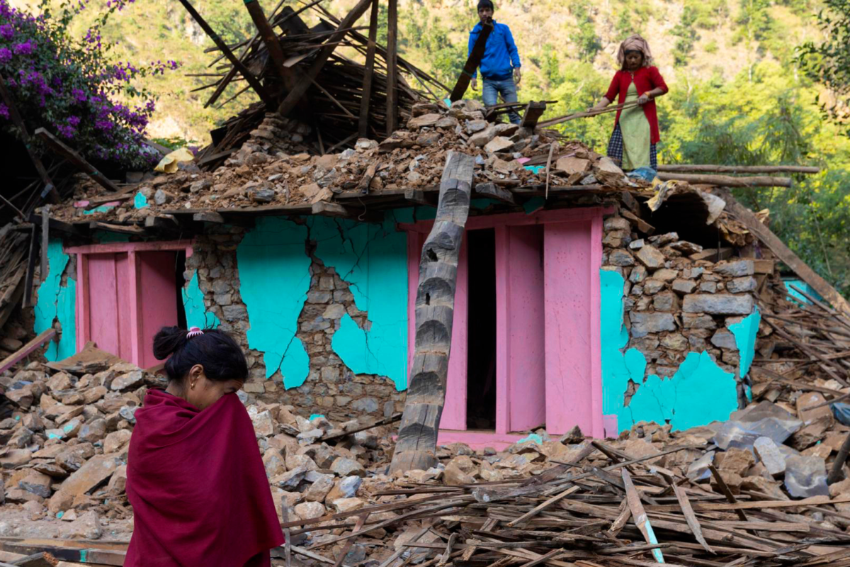 Meisje huilt voor verwoest huis, twee mensen staan bovenop de schade en proberen het op te ruimen.