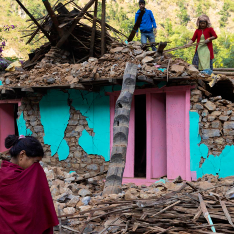 Meisje huilt voor verwoest huis, twee mensen staan bovenop de schade en proberen het op te ruimen.